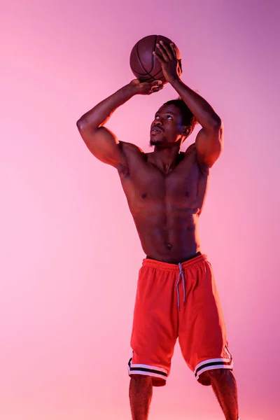 Guapo, musculoso afroamericano deportista jugando baloncesto en rosa y púrpura gradiente fondo — Stock Photo