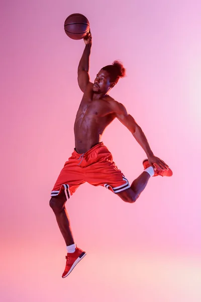 African american sportsman with muscular torso playing basketball on pink and purple gradient background — Stock Photo
