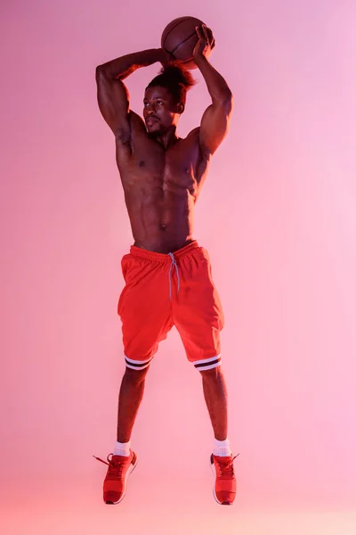 Handsome, muscular african american sportsman playing basketball on pink and purple gradient background — Stock Photo