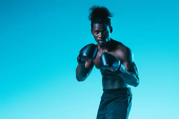 Confident african american boxer with muscular torso looking at camera on blue background — Stock Photo