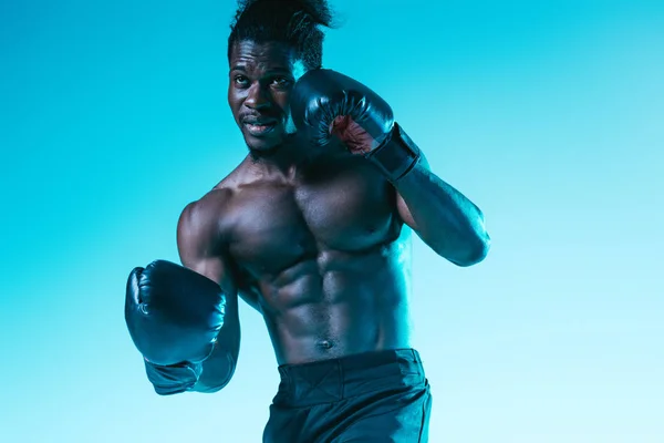 Handsome, muscular african american sportsman boxing on blue background — Stock Photo