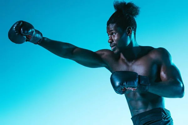 Confiante desportista africano no treinamento de luvas de boxe em fundo azul — Fotografia de Stock