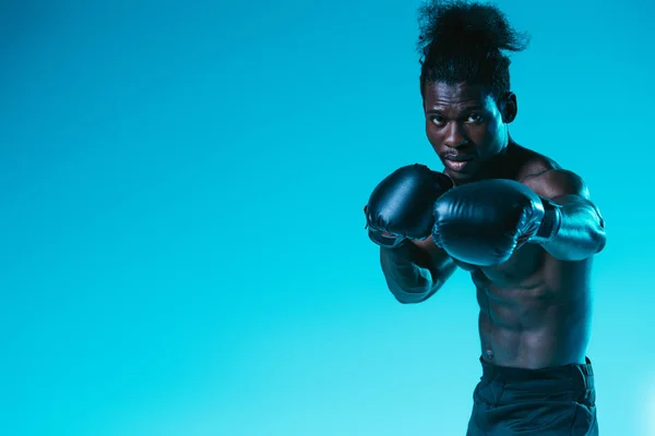 Uomo sportivo afroamericano senza maglietta in guanti da boxe guardando la fotocamera su sfondo blu — Foto stock