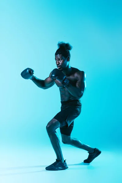 Confident african american sportsman in shorts and sneakers boxing on blue background — Stock Photo