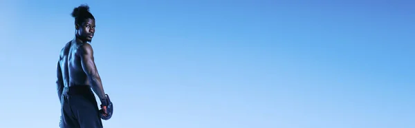 Panoramic shot of shirtless, muscular african american boxer looking at camera on blue background — Stock Photo