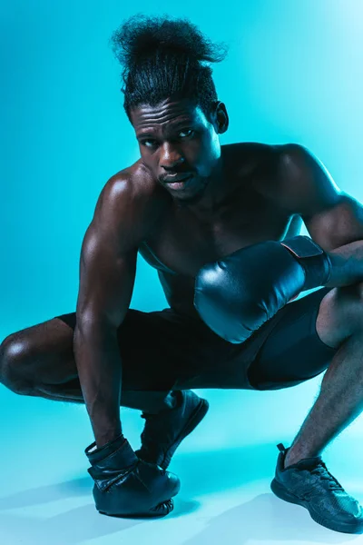 Впевнений, м'язистий афроамериканський спортсмен в боксерських рукавичках позує на камеру на синьому фоні — стокове фото