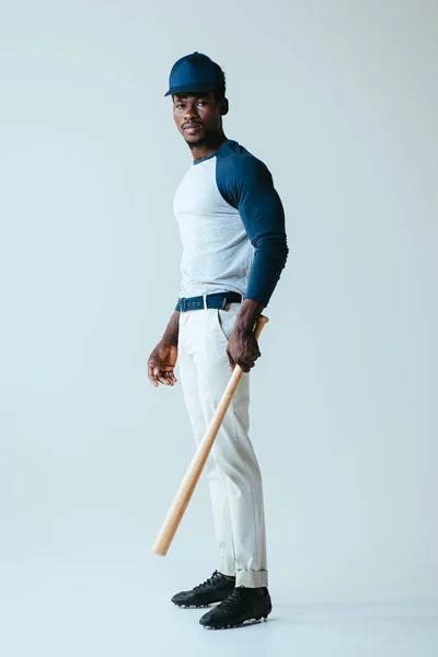 Handsome african american sportsman holding baseball bat while looking at camera on grey background — Stock Photo