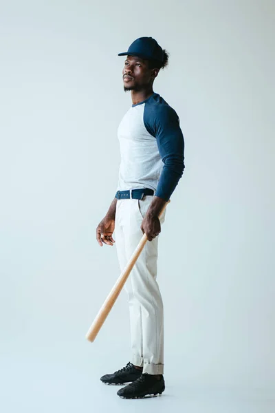 Handsome african american sportsman looking away while holding baseball bat on grey background — Stock Photo