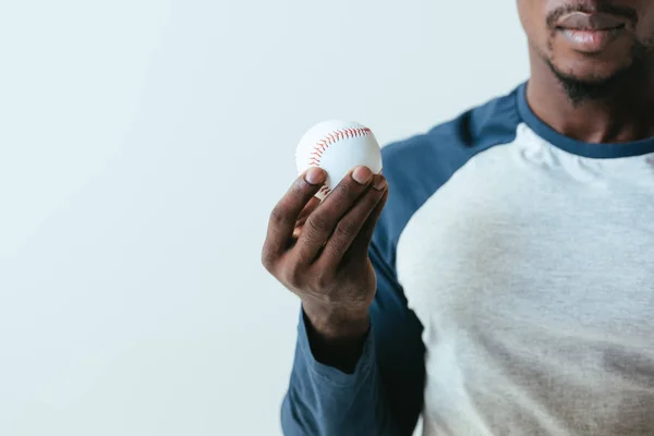 Vista parcial del jugador de béisbol ameriqueño africano sosteniendo la pelota aislada en gris - foto de stock