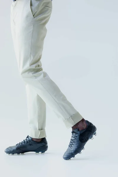 Vista recortada del jugador de béisbol amrica africano en pantalones blancos y zapatillas de deporte sobre fondo gris - foto de stock