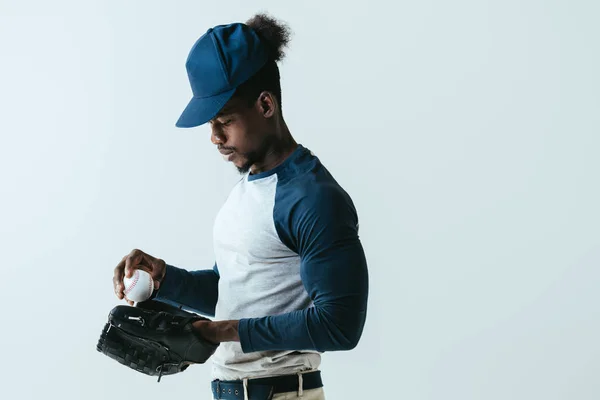 Guapo afroamericano deportista en el guante de béisbol sosteniendo bola aislado en gris - foto de stock