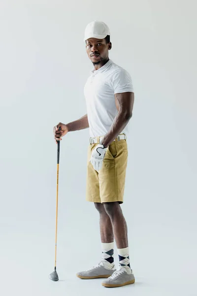 Bell'uomo sportivo afro-americano che tiene il golf club su sfondo grigio — Foto stock