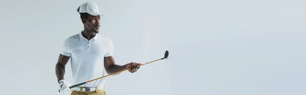 Plano panorámico del apuesto deportista afroamericano sosteniendo club de golf aislado en gris - foto de stock