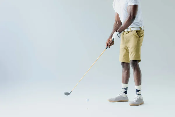 Vista recortada del deportista afroamericano en pantalones cortos jugando al golf sobre fondo gris - foto de stock