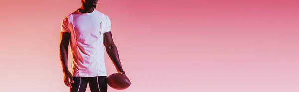 Partial view of african american sportsman holding rugby ball on pink background with gradient, panoramic shot — Stock Photo