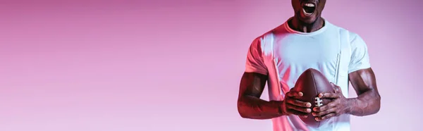 Partial view of african american sportsman screaming while holding rugby ball on purple background with gradient, panoramic shot — Stock Photo