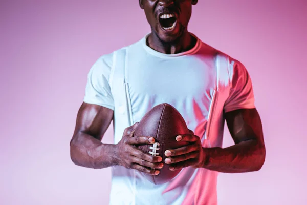 Cropped view of african american sportsman yelling while holding rugby ball on purple background with gradient — Stock Photo