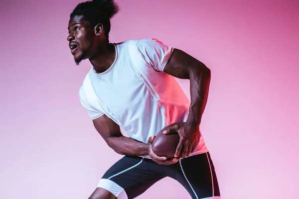 Emocionado deportista afroamericano jugando fútbol americano sobre fondo púrpura con gradiente - foto de stock
