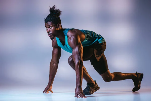 Athletischer afrikanisch-amerikanischer Sportler steht in Startposition auf grauem Hintergrund mit Beleuchtung — Stockfoto