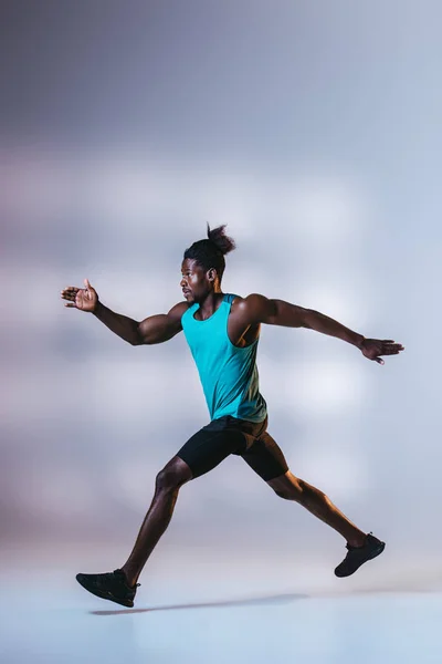 Jovem esportista afro-americano correndo em fundo cinza com iluminação — Fotografia de Stock