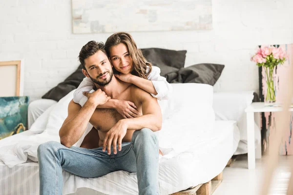 Enfoque selectivo de la joven pareja abrazándose mientras está sentado en la cama y mirando a la cámara — Stock Photo