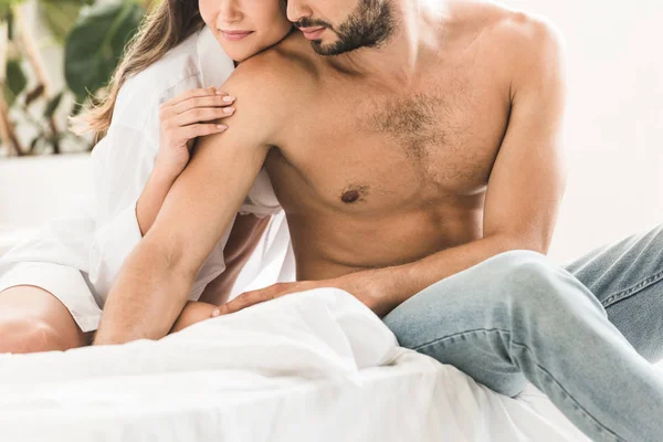 Recortado vista de sexy pareja sentado en la cama y cogido de la mano - foto de stock