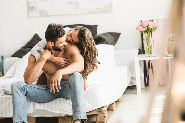 Jovem casal abraçando enquanto sentado na cama e olhando uns para os outros — Fotografia de Stock