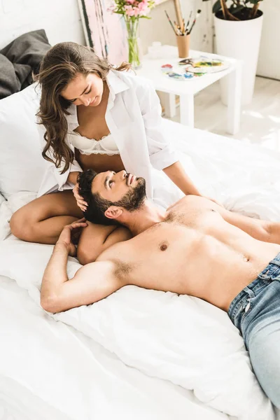 Hombre sin camisa acostado en las rodillas de la novia mientras que la chica sentada en la cama y mirando al chico - foto de stock