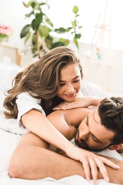 Casal sexy deitado na cama perto um do outro e sorrindo ao abraçar — Fotografia de Stock