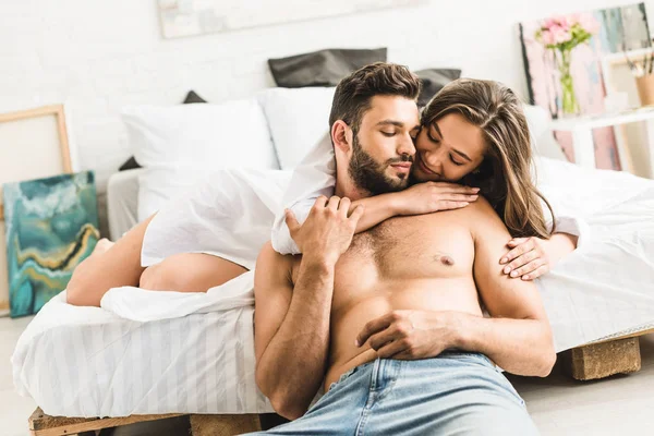 Young girl lying in bed and hugging man while guy sitting on floor near bed — Stock Photo