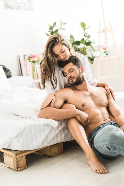 Sexy homme torse nu assis à côté lit et fille étreignant petit ami de dos — Photo de stock