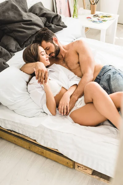 Sexy young couple hugging while lying in bed and holding hands — Stock Photo