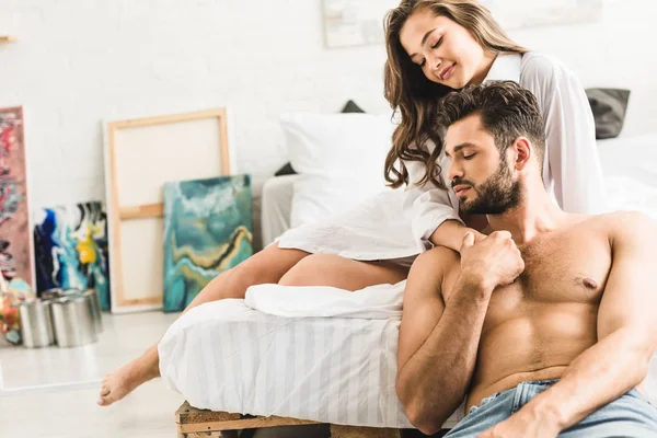 Joven hombre y chica sonriendo mientras toma de la mano y se sienta en la cama - foto de stock