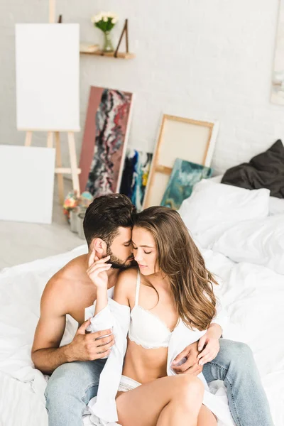 Sexy pareja sentado en la cama mientras hombre tratando de beso chica en el cuello - foto de stock