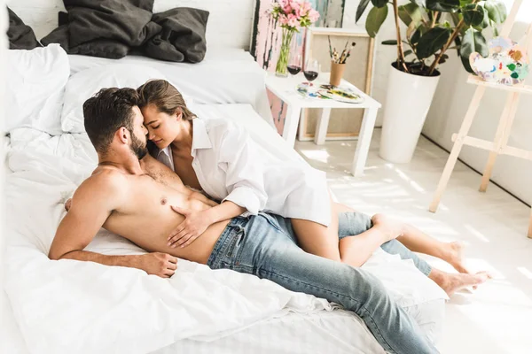 Ganzkörperansicht des sexy jungen Paares, das im Bett liegt, während Mädchen den Oberkörper des Mannes berührt — Stockfoto