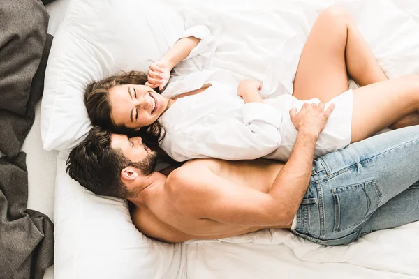 Sexy pareja acostada en la cama y riendo mientras hombre abrazando chica desde atrás - foto de stock