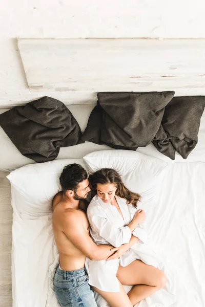Top view of sexy couple lying on bed while man hugging girl from back — Stock Photo