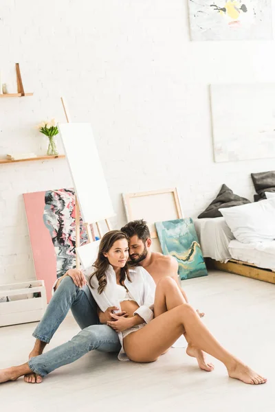 Vista de longitud completa de sexy pareja sentada en el piso en el dormitorio - foto de stock