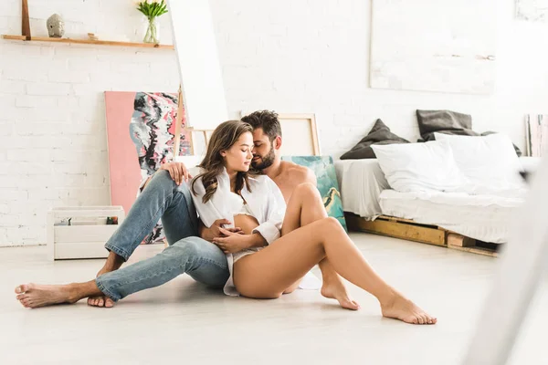 Selective focus of sexy couple sitting on floor while man hugging girl from back — Stock Photo