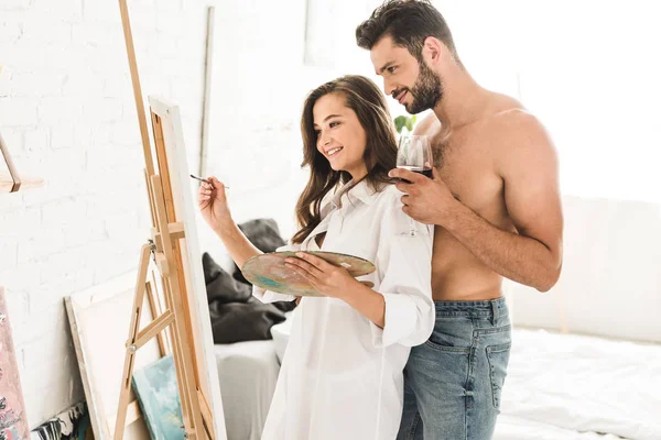 Sexy homem de pé atrás namorada enquanto menina desenho com escova — Fotografia de Stock