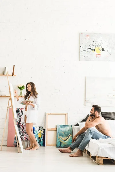 Visão de comprimento total da menina desenho com escova e homem sorrindo enquanto sentado na cama — Fotografia de Stock