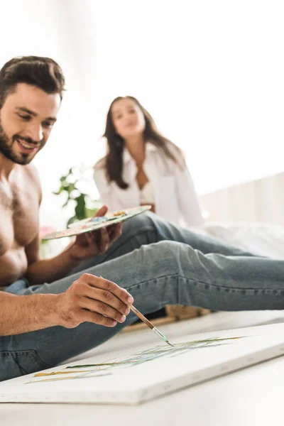 Selective focus of man drawing while sitting on floor and girl sitting in bed — Stock Photo