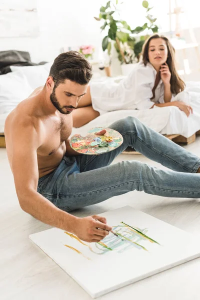 Messa a fuoco selettiva di disegno uomo mentre seduto sul pavimento e ragazza sdraiata a letto — Foto stock