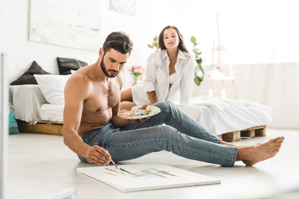 Selective focus of couple sitting in bedroom while man drawing and girl looking at guy — Stock Photo