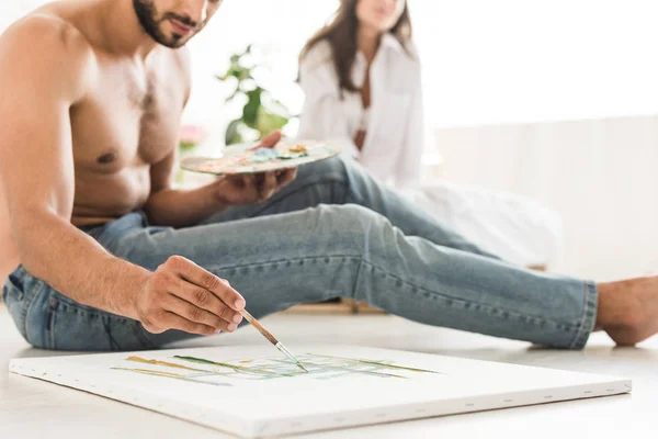 Ausgeschnittene Ansicht eines Mannes, der mit Pinsel zeichnet, während er auf dem Boden sitzt und eines Mädchens, das im Bett sitzt — Stockfoto