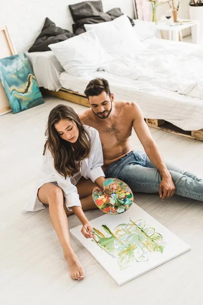 Vista ad alto angolo di coppia felice seduta sul pavimento, mentre la ragazza paiting e l'uomo guardando processo — Foto stock