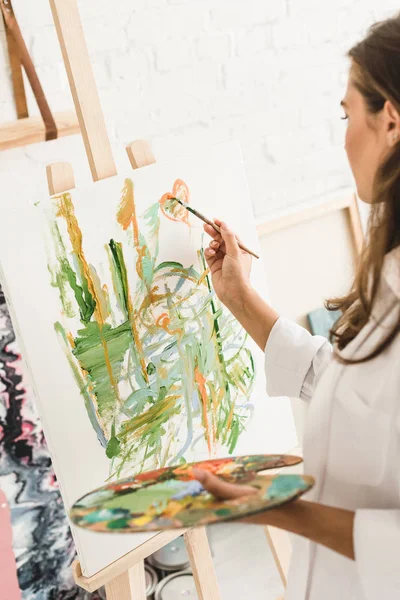 Selective focus of young girl drawing with brush and holding palette — Stock Photo