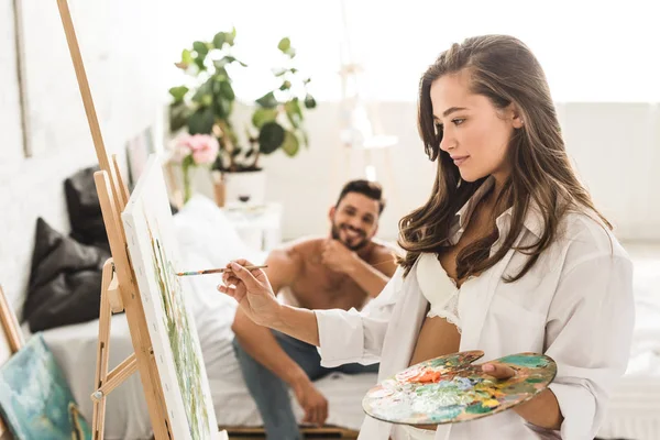 Messa a fuoco selettiva della ragazza sexy in biancheria intima bianca e disegno camicia mentre l'uomo senza maglietta sorridente e seduto a letto — Foto stock