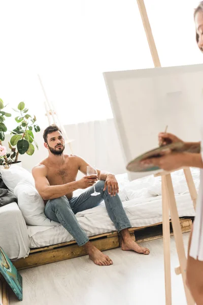 Selektiver Fokus des Mannes, der mit Wein im Bett sitzt, und des Mädchens Zeichnung mit Pinsel — Stockfoto