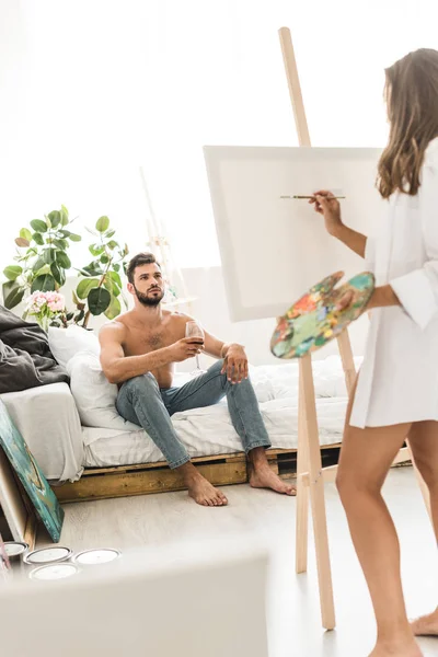 Foyer sélectif de l'homme assis dans le lit avec du vin et fille dessin gars — Photo de stock